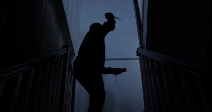 A thief in a black cloak and gloves sneaks into a house at midnight, holding a knife and flashlight, with the intent to harm the occupants.