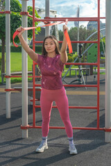 Asian girl exercising with a rubber expander on a street sports ground. Sport and Recreation.
