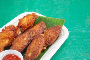 Golden fried chicken wings served with sauce on biodegradable tray.