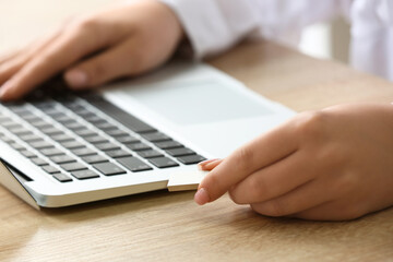 Woman with modern laptop and USB flash drive at wooden table, closeup