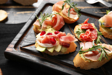 Board of tasty bruschettas with ham on dark wooden background, closeup