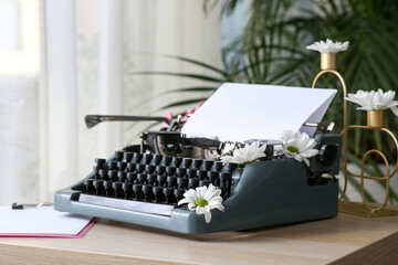 Vintage typewriter with paper sheet and flowers on wooden table in room