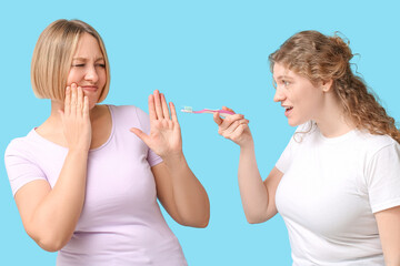 Beautiful women with teeth brush suffering from toothache on blue background