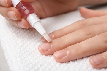 Female hands applying cuticle oil onto fingernails on white towel, closeup
