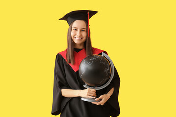 Young female graduate with globe on yellow background