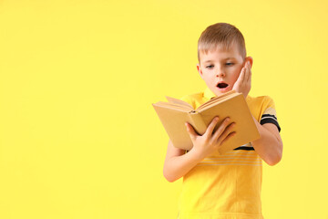 Shocked little boy with book on yellow background