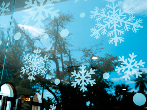 Merry Christmas and Happy New Year concept. Many Christmas snowflake sticker decoration on window glass in cafe with blue sky background and trees, reflection from outside.