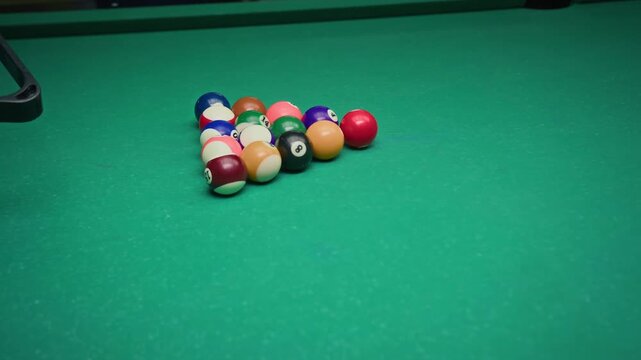 Slowmo of unrecognizable Black male player arranging colorful balls on green table in triangle and breaking in, starting game of pool