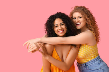 Fototapeta premium Beautiful young women hugging on pink background