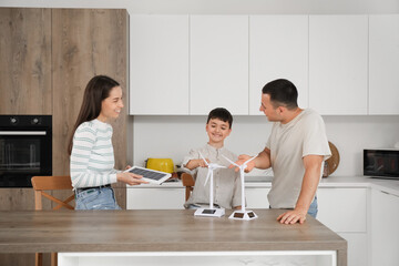 Happy family with wind turbine models and portable solar panel in kitchen