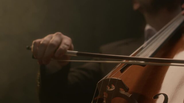 Cropped shot of unrecognizable male musician in suit performing music with cello on black background
