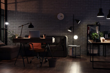 Interior of dark office with workplace and glowing lamps
