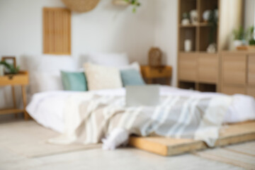 Blurred view of bedroom with laptop on big bed, drawers and plants