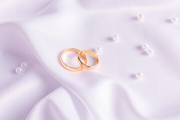 A pair of classic gold rings on white satin with a scatter of pearls. The concept of the wedding. postcard, invitation, wallpaper. wedding background.