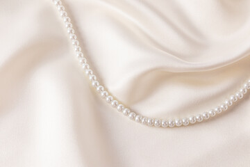 Chic wedding background beige, cream satin with soft waves of fabric and string of pearl beads. A...