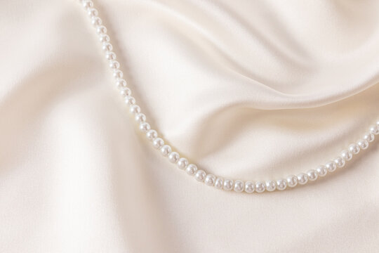 Chic wedding background beige, cream satin with soft waves of fabric and string of pearl beads. A copy of the space. cover, postcard, album.