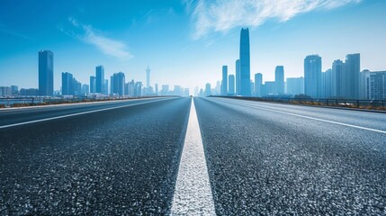 Obraz premium A clear view down a smooth highway leading towards a modern city skyline under bright blue skies, capturing the essence of urban progress and connectivity.