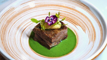 Gourmet dish of tender beef short rib with vibrant green sauce, edible flower and artistic garnish plated in fine dining presentation on ceramic plate, Culinary Art and Fine Dining.