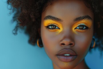 Black woman with colorful eye makeup standing against blue backdrop.