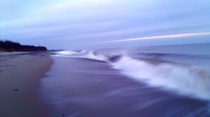 Fototapeta premium A clear picture of a sandy beach with a breaking wave and a distant cliff