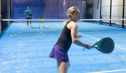  A woman is playing padel, hitting a ball on a bright blue court, 