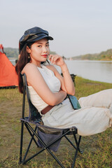 Fototapeta premium Elegant young Asian woman is sitting in a lawn chair by a lake.