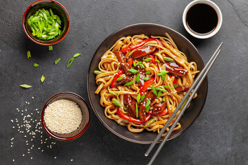 Udon stir fry noodles with beef meat and vegetables in a bowl on dark background. Asian cuisine. Delicious and healthy food. Top view