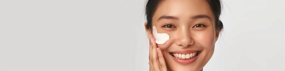 Asian woman is applying makeup to her face. She is smiling and she is happy. Concept of self-care and confidence