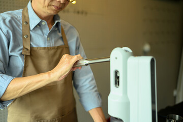 Asian senior man barista wearing apron preparing coffee in a modern coffee shop