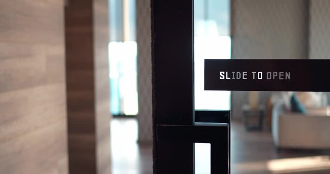 Door with sign slide to open opened silently and smoothly. Woman walked through glass door into spacious room, having crossed threshold. Concept of simplicity and convenience in modern door design.