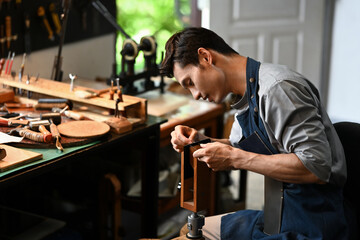 Portrait of talented artisan sitting at his workbench surrounded by various tools and materials essential for leather crafting