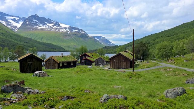 A serene video of a village nestled in the mountains, with a lake, lush greenery, grasscovered roofs, and towering mountains, creating a tranquil setting Innderalen Norway