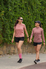 Two Latin Women Walking and Laughing by Green Wall
