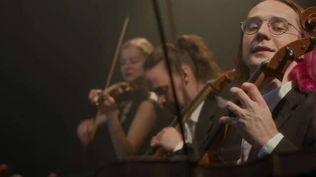 Tilt down shot of symphonic string quartet giving acoustic music concert on stage, playing with elegance and passion