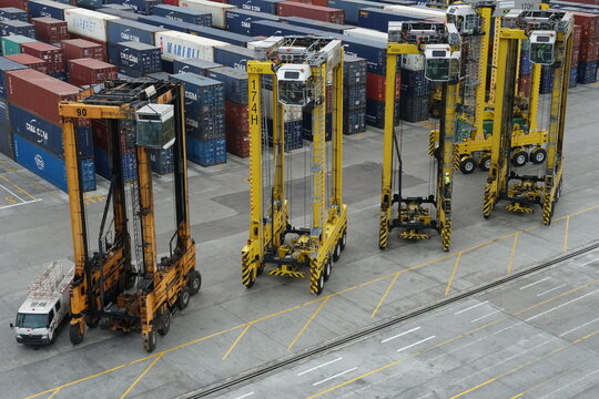 Kingston, Jamaica - 05 29 2024: Several yellow straddle carriers in a row in Kingston Freeport container terminal waiting under the gantry crane. There are many of other boxes from shippers.