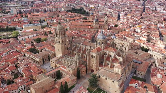 Drone view of historic area of Spanish city of Salamanca with brownish tiled roofs of old houses, gothic building with baroque dome of medieval cathedral and La Clerecia on sunny spring day