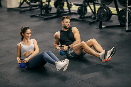 Strong muscular sportspeople doing russian twist with kettlebell at gym.