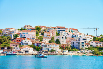 Naklejka premium Seaside town with colorful coastal houses on hillside with boats docked along clear blue waters. Residential apartments for summer vacation on Adriatic Sea in Rogoznica, Croatia