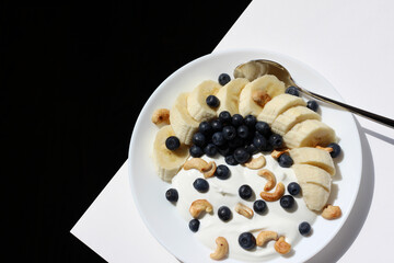 Breakfast Food. Plate of Greek Yogurt with Fresh Blueberries, Cashew Nuts, and Banana, Served on Table.