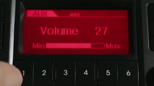 A hand reaches towards a car radio and adjusts the volume up to , as indicated by the display