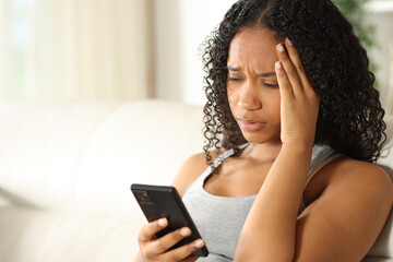 Worried black woman checking phone at home