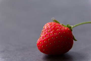Fresh red strawberry with glossy texture on gray background. Healthy food, fruit still life, kitchen decoration concept.