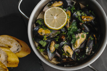 Mussels in white wine with parsley and lemon in a saucepan on a gray table. Close-up. Mediterranean cuisine, traditional French recipe.