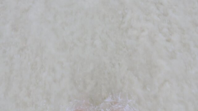 Feet standing on sandy beach as ocean waves roll in from above