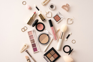 Flat lay of assorted makeup products including lipstick, blush, and brushes on a beige background
