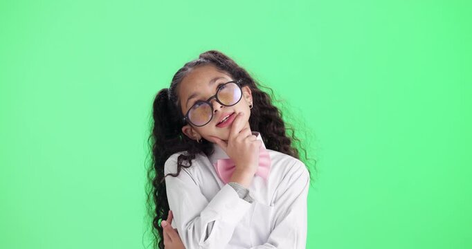 Child, girl and thinking with glasses on green screen for decision, choice or intelligence in education and learning. Young student or kid with idea, solution or guessing in quiz on studio background