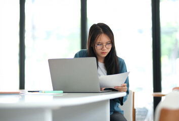 A woman is sitting at a desk with a laptop and a piece of paper