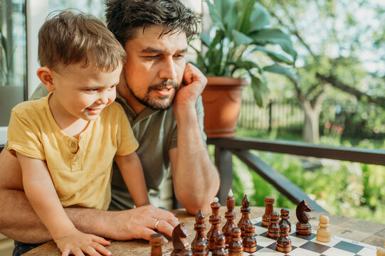 Father and son spending leisure time playing chess sitting on porch