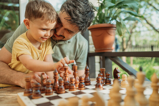 Happy father sitting with son playing chess on porch