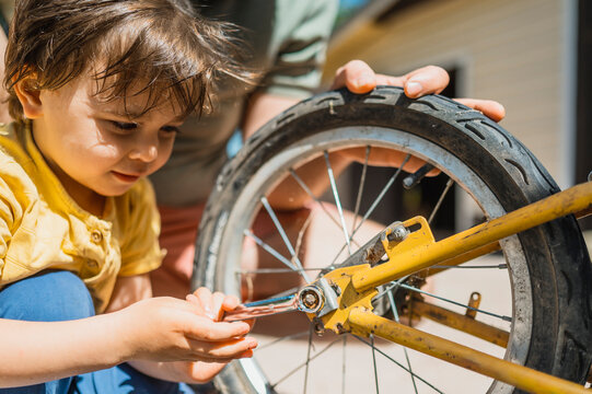 Son fastening bicycle wheel using wrench in back yard